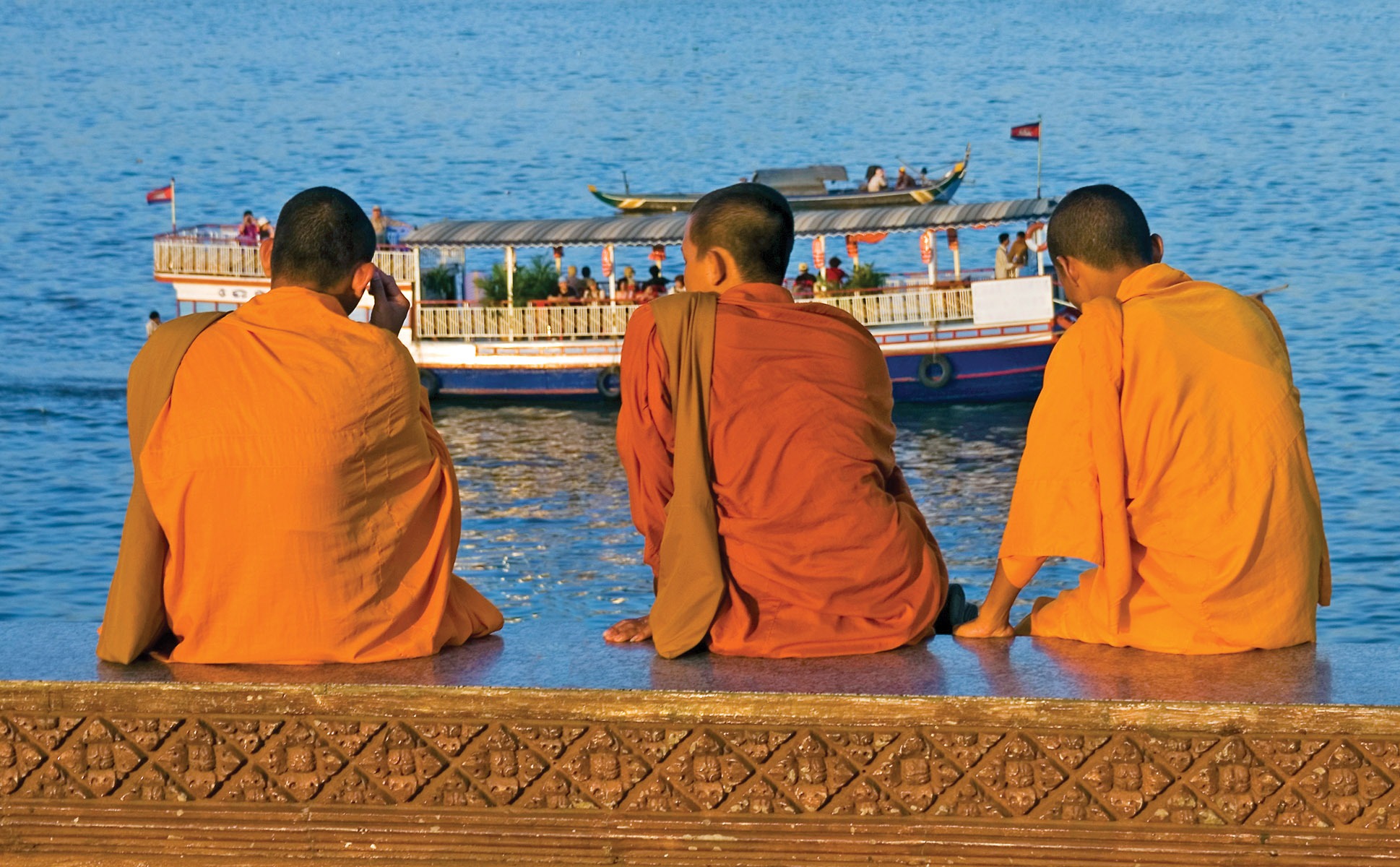 Three Monks Sitting Next to the Mekong River with a Riverboat Passing