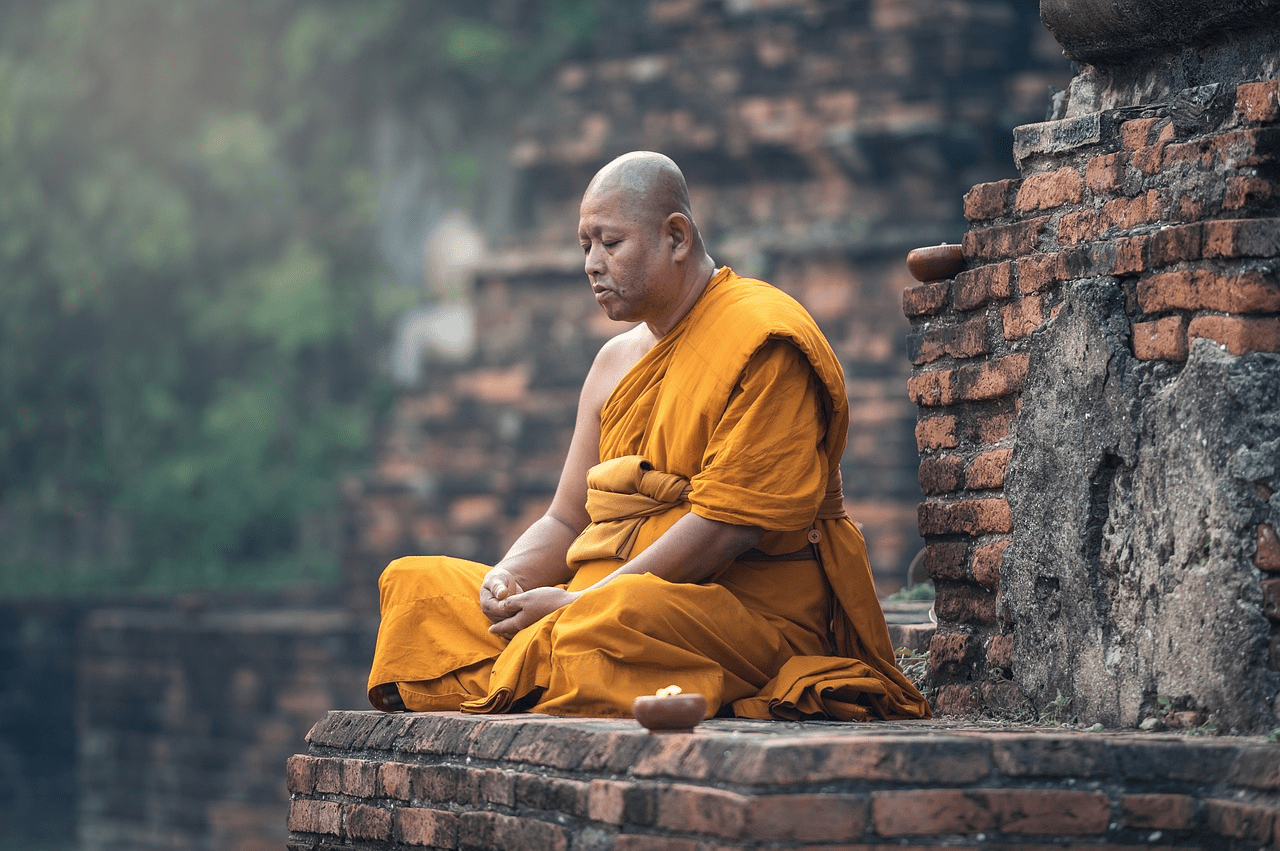 A Buddhist Monk Meditating in Traditional Saffron Robes Near Ancient Brick Ruins in a Peaceful Outdoor Setting