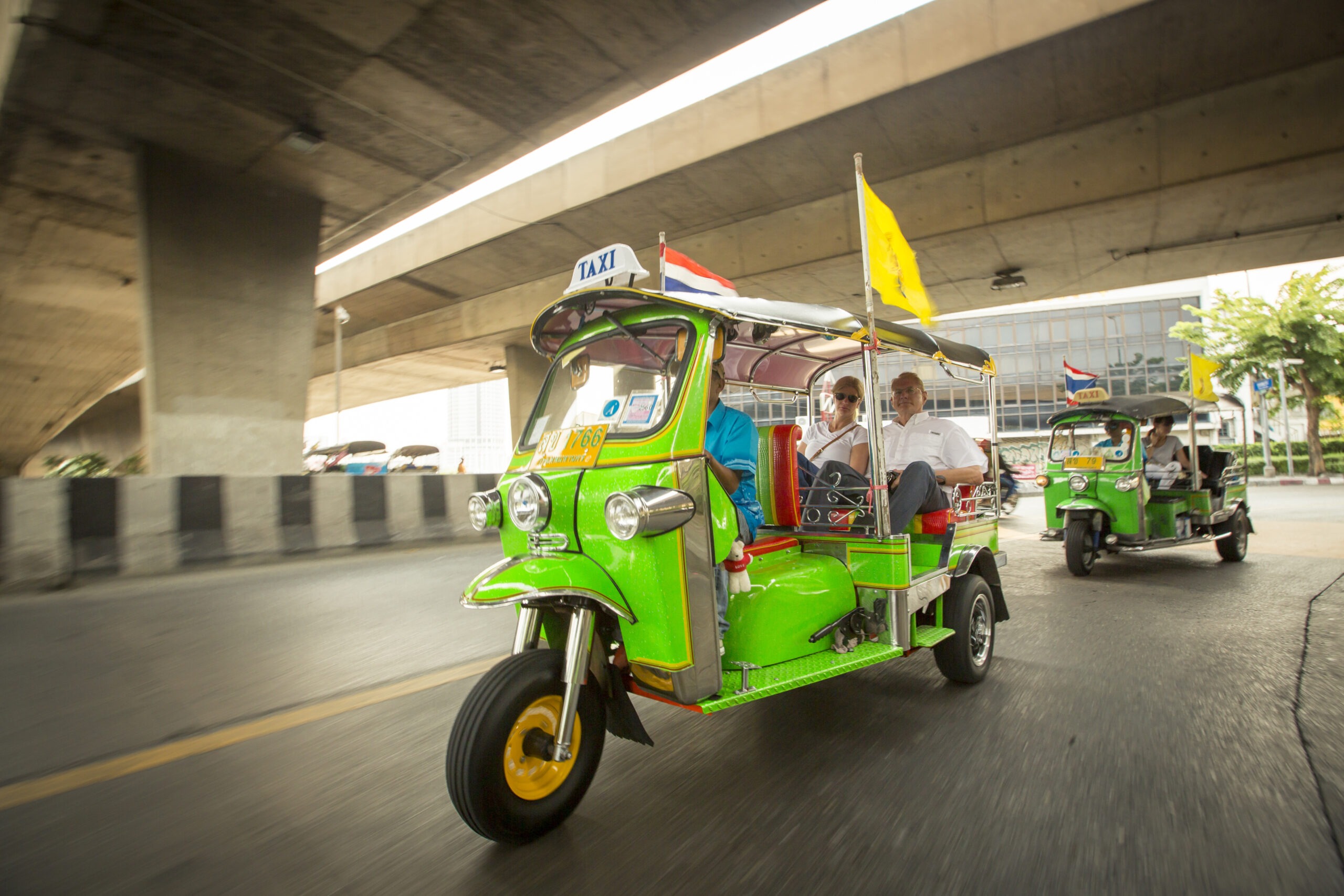 Tourists Riding in a Green Tuk-Tuk Taxi Under a Bridge in Bangkok
