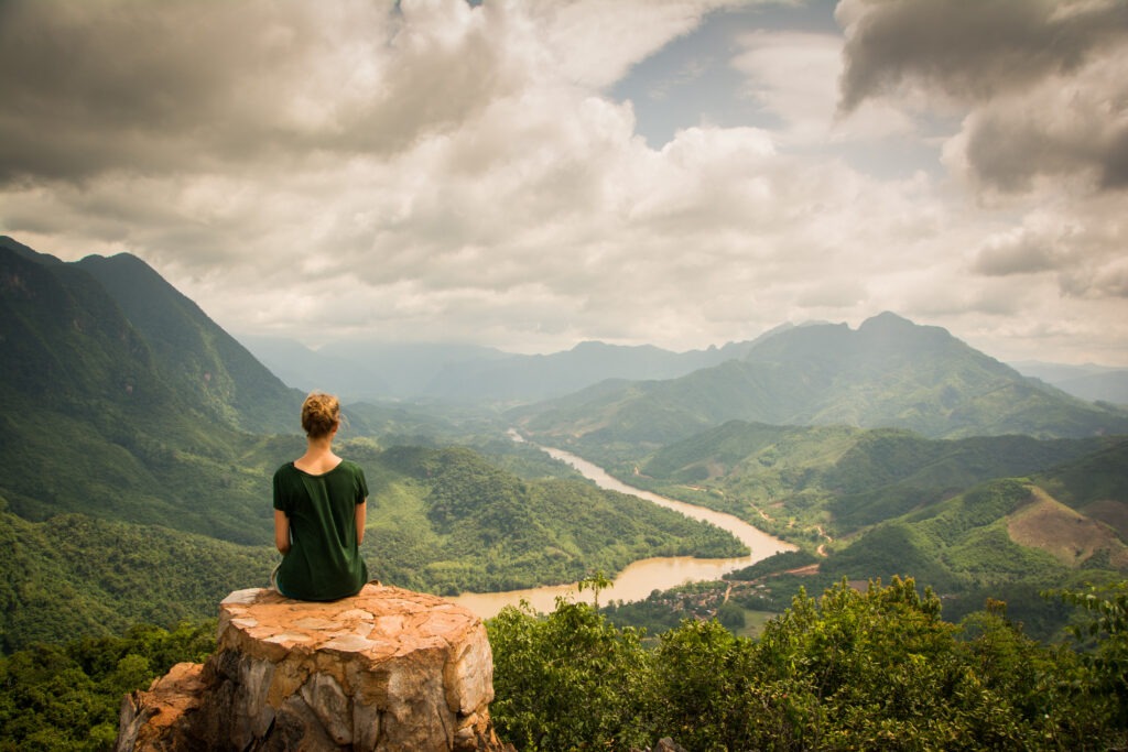 Girl With Green Shirt Sitting on a Rock on Top of a Mountain